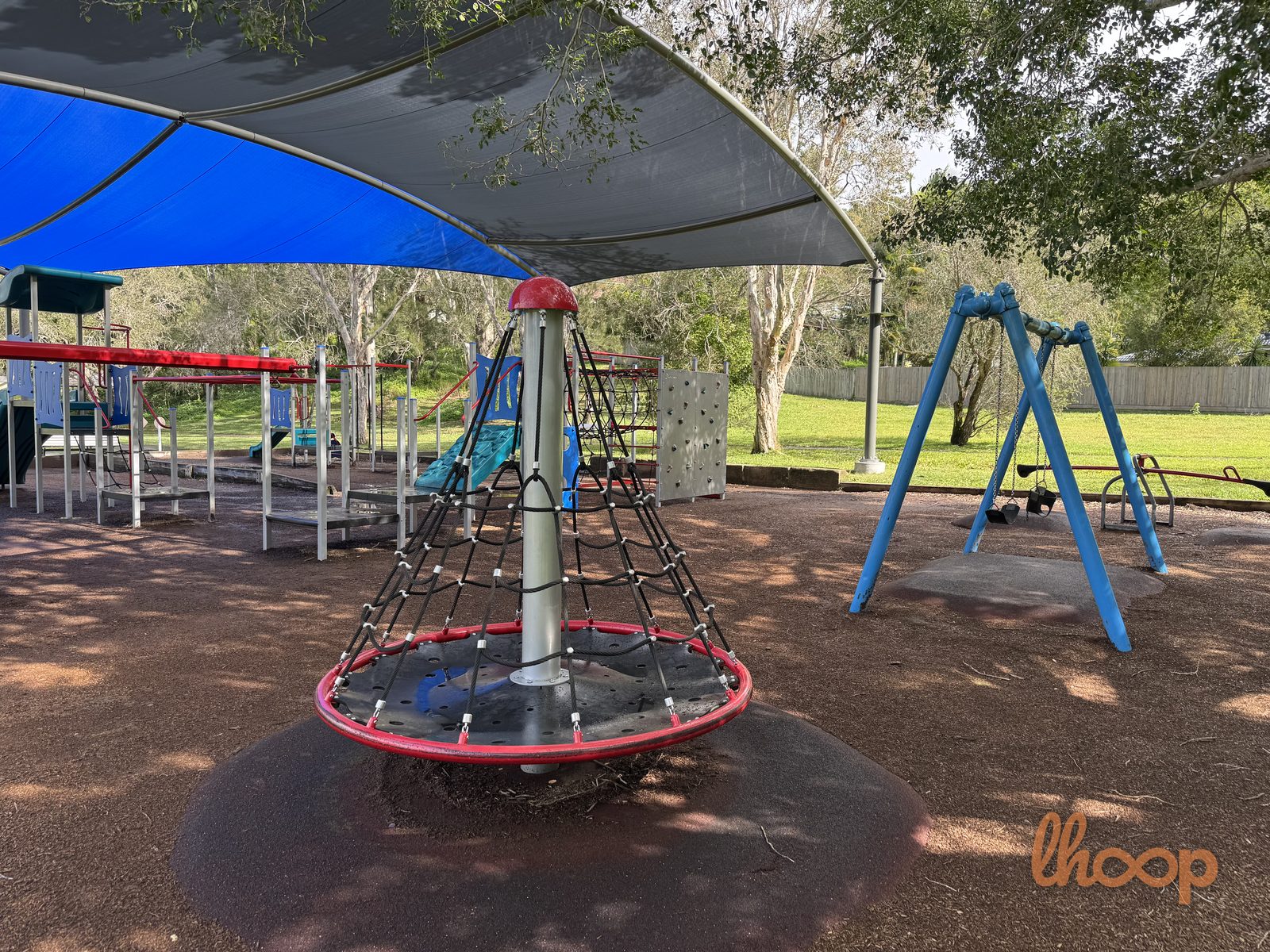 A cone-shaped rope spinner and a blue swing set with a toddler seat under the shade sail.
