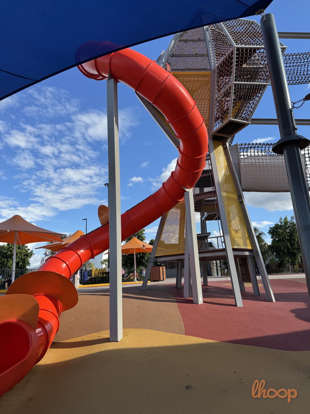 A winding red tube slide dropping from the tallest play tower.