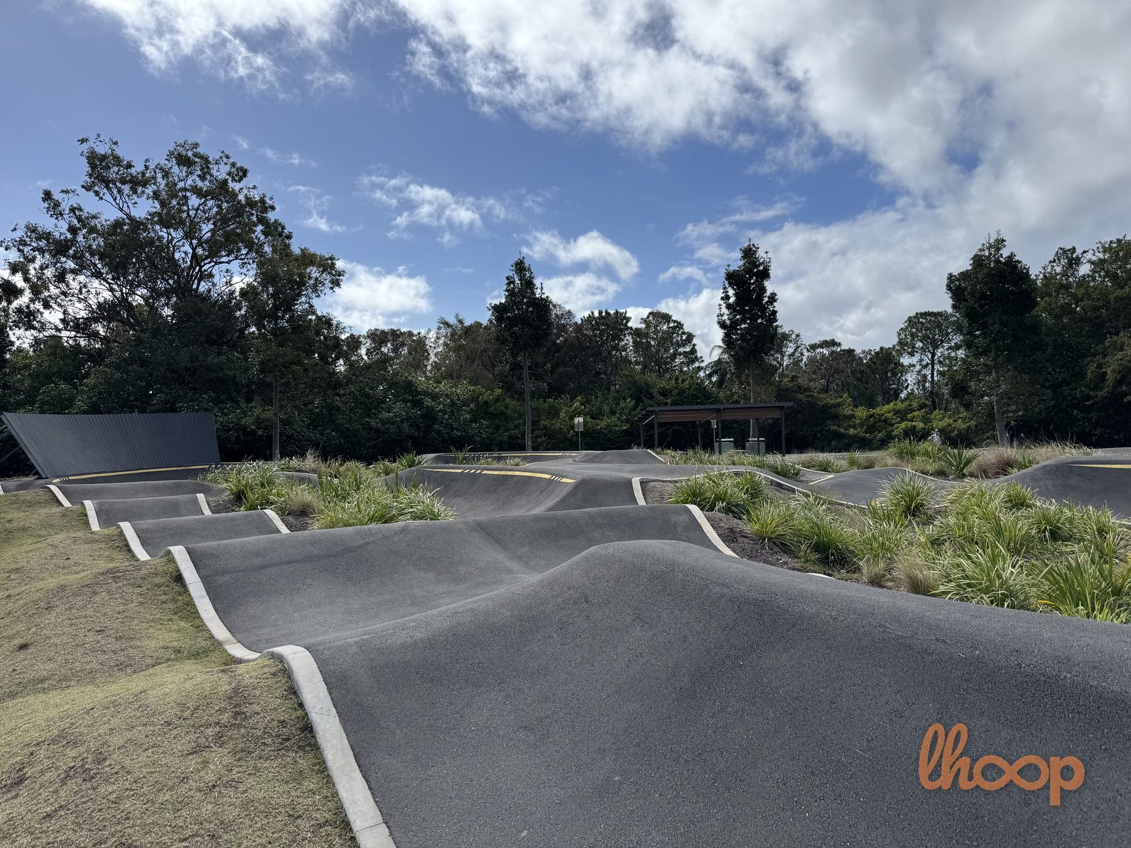 A rhythm section of repeating rollers running along the edge of the pump track, with a wave-wall ramp to the left.